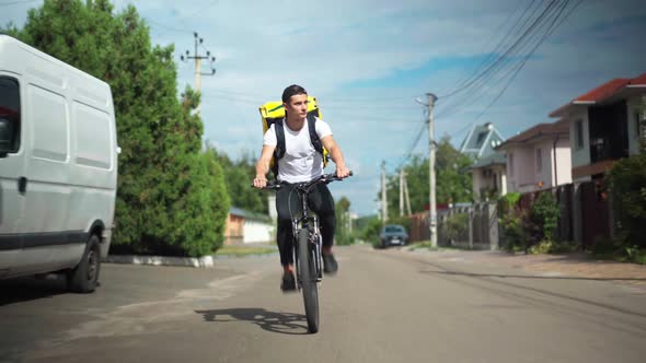 Wide Shot Front View Confident Delivery Boy Driving Bicycle Fast on Sunny Street in Town alt