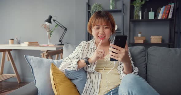 Asia lady using smart phone video call talk with family on sofa in living room at house.