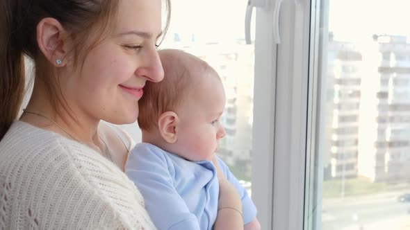 Portrait of Smiling Mother with Little Baby Son Looking on City Street Through Window alt