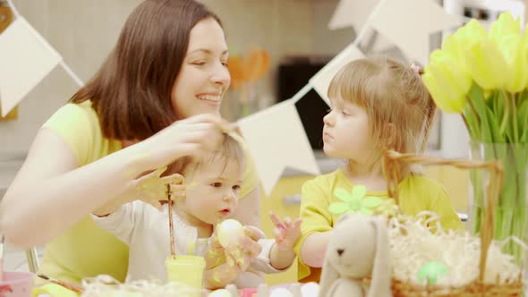 Happy easter. A mom and her two baby girls painting Easter eggs at kitchen