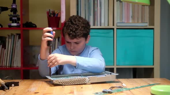 Schoolboy boy unscrews chip with screwdriver to work with soldering iron.