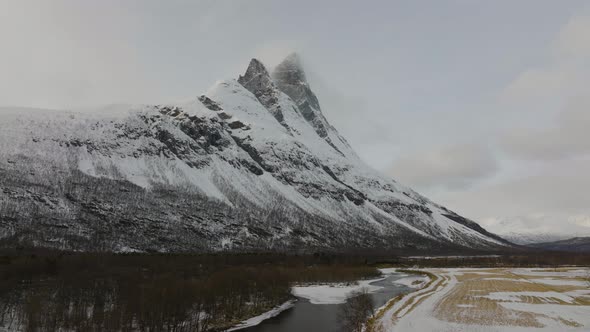 Flying over the forest and river towards the snow covered Otertinden mountain summit in northern Nor alt