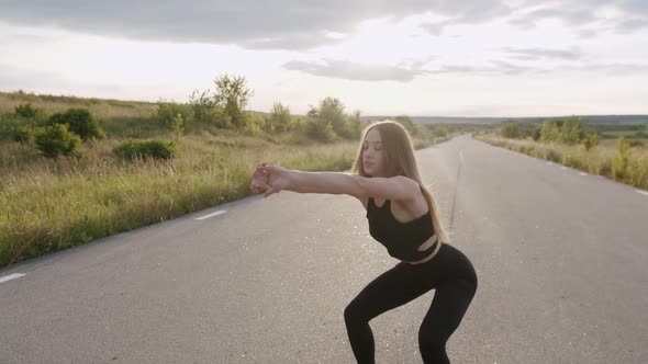 Pretty Athletic Girl Doing Squats and Warmup on the Road at Nature with Sunset alt