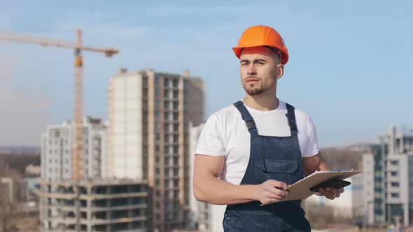 The Young Engineer is Holding a Folder of Documents and a Smartphone alt