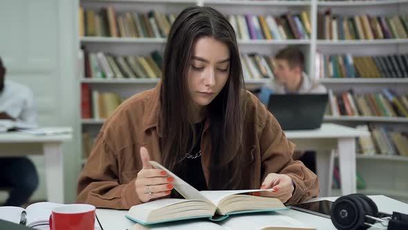 Modern Young Woman with Long Hair Reading Book in the University Library and then Looking Aside alt