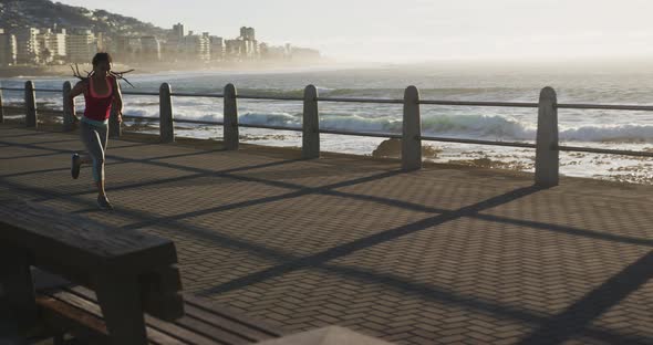 African american woman running on promenade by the sea at sundown alt