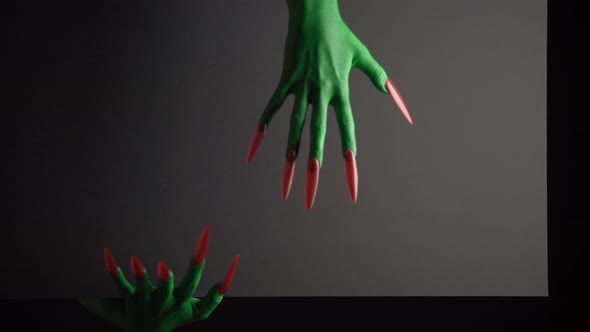 Green Witches Hands Appears From Behind a Black Background with Copyspace