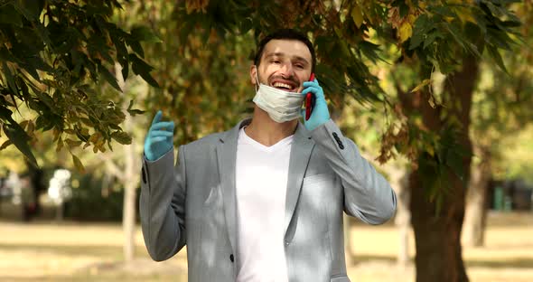 Bearded young man talking phone and pushing his face mask to his chin.