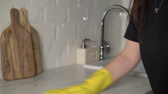 A Housewife in Yellow Rubber Gloves Washes and Wipes a Marble Kitchen Countertop
