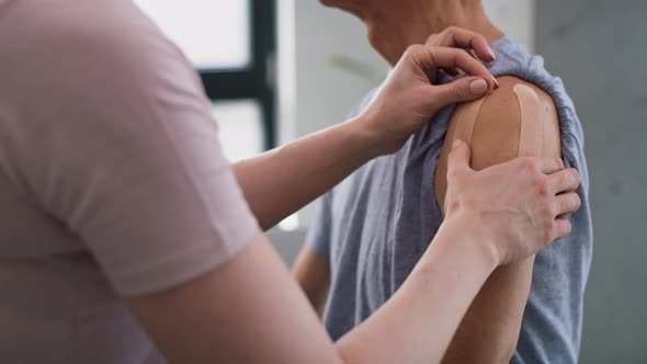 Physical therapist applying kinesio tape on senior patient's arm. Shot with RED helium camera in 8K. alt