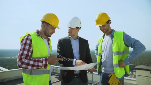 Young Male Boss in Safety Helmet Discussing Construction Plan With Workers