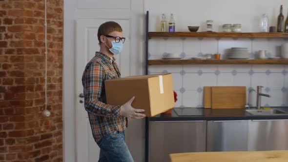 Guy in Protective Wear Holding Delivery Box at Home alt