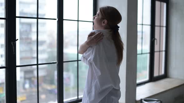 city dweller yawns early in morning in front of a window overlooking the city alt