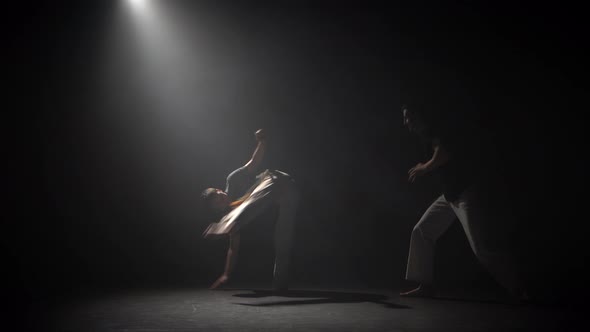 Handsome Males Practicing Capoeira in Darkness Against Spotlight in Studio alt