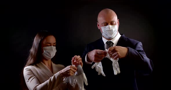 Portrait of a Couple in Business Clothes on a Black Background. They Put Disposable Masks on Their alt