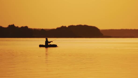 Golden sunset and the silhouette of a man throwing a fishing rod from the boat.  alt