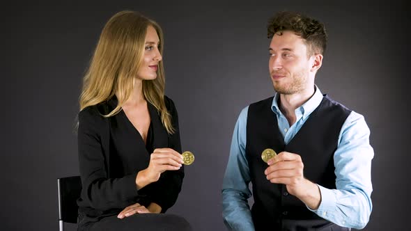 Sitting business couple exchange looks and shows cryptocurrency coins. alt