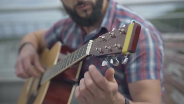 Close-up of Guitar Fingerboard with Blurred Bearded Man Playing Musical Instrument. Unrecognizable alt