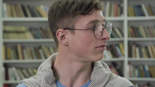 Handsome Smiling Smart Guy in Glasses Looking at Camera in the Library alt
