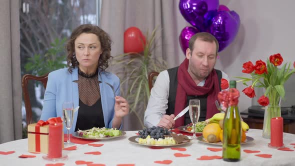 Angry Caucasian Man Standing Up From Valentine's Dinner Table and Leaving Woman Alone Passing Camera alt