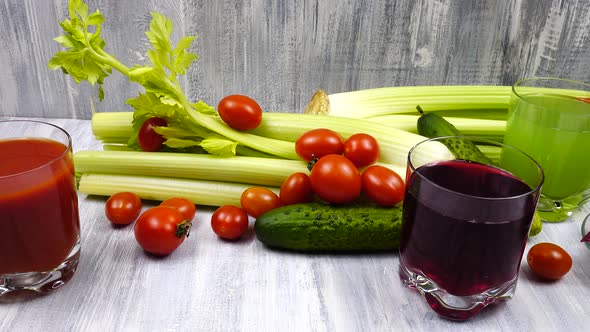 Glasses of tomato, celery, and beets juice stand on a wooden table