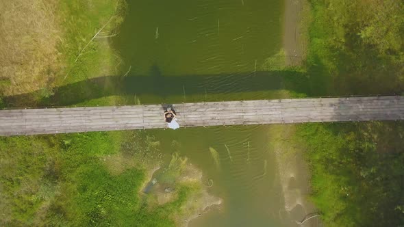 Camera Turns Above Newly Wedded Couple on Old Wooden Bridge alt