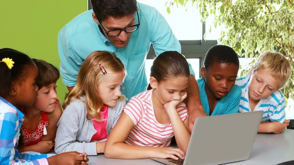 Teacher and kids using laptop in classroom alt