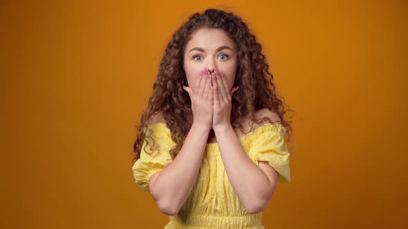 Surprised Young Woman Covering Mouth in Shock Against Yellow Background