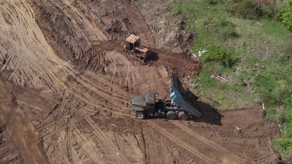 Aerial shot of tipper unloading ground on further construction site. alt