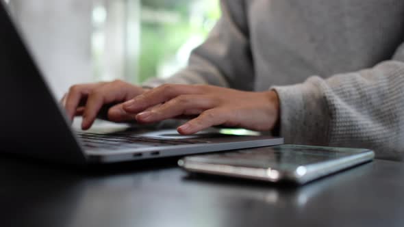 a woman touching and scrolling on smart phone screen while working on laptop computer