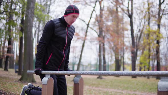 A Young Man Does Push Ups on a Pole in a Park. alt