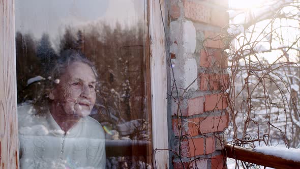 an Elderly Woman in Her House Looks Out of a Window with Glare Her Brick House on a Winter Garden in alt