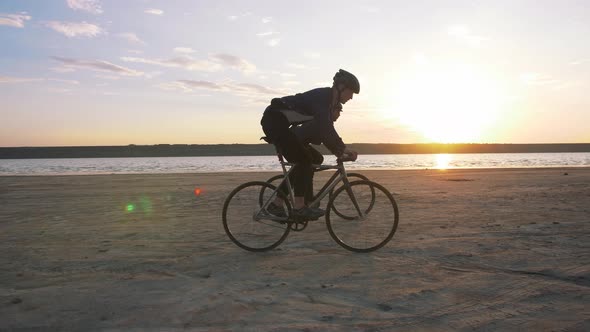 Two Young Men Riding Bicycles on the Beach on the Background of an Orange Sunsetting Sky alt