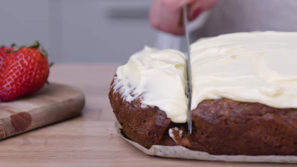Lady Slicing Her Baked Carrot Cake With Fresh Strawberries In A Wooden Chopping Board - slider right alt