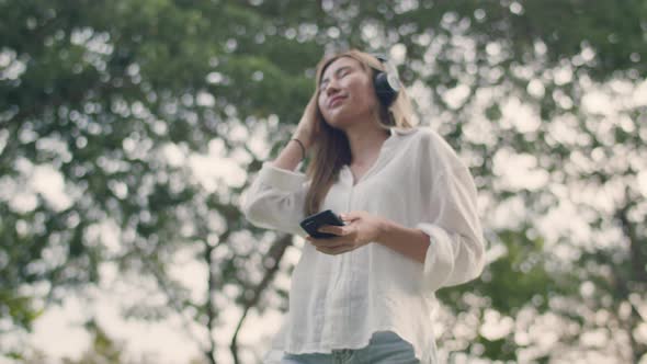 Asian woman enjoying the breeze outdoors and having fun wearing headphones listening to music.