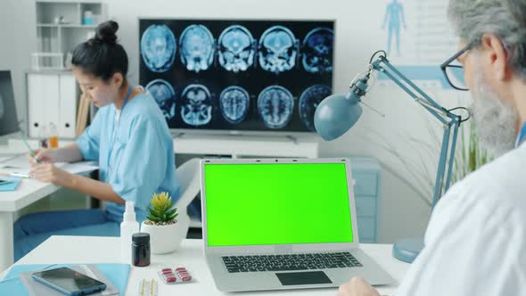 Doctor Using Chroma Key Green Screen Laptop While Nurse Writing Medical Records in Hospital alt