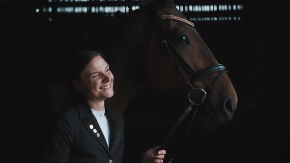 Joyful Girl Laughing And Posing With Her Horse In The Stable Holding Its Rope alt