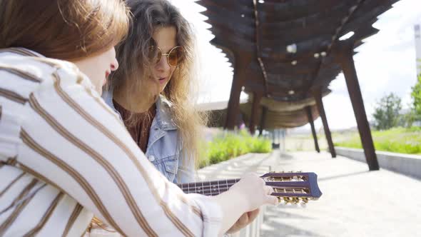 Woman Teaches Friend to Play Ukulele in Park on Sunny Day