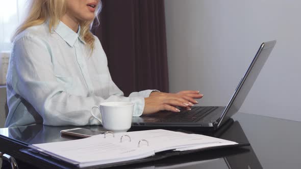 A Woman Reads Important Documents in a Folder and Types It Into a Laptop