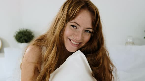 Young woman sits relaxed on the bed and hugs a soft, pillow