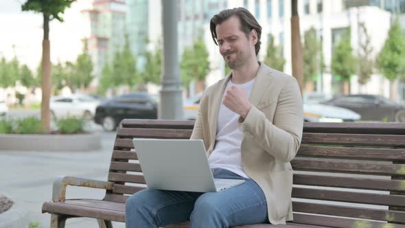 Young Man with Wrist Pain Using Laptop While Sitting on Bench alt