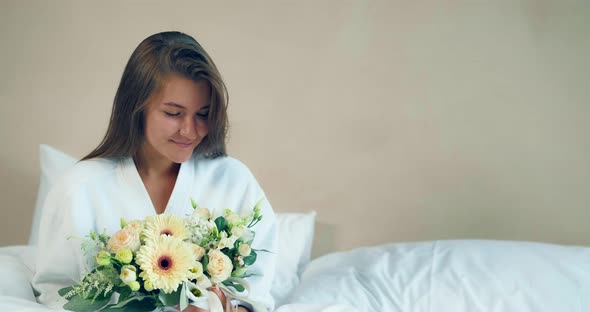 Pretty Woman Holds Nice Flowers Bouquet Sitting on Soft Bed