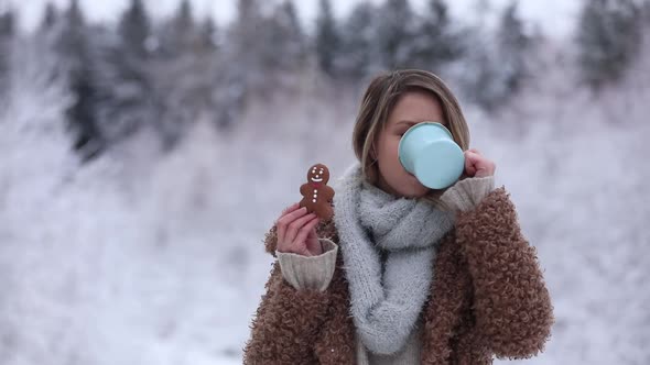 Beautiful girl in coat with cup of hot drink in a snow forest. alt
