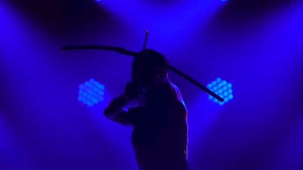Silhouette of Dancing Joan of Arc with Bow and Arrow on Stage in a Dark Studio with Smoke and Neon alt