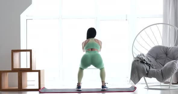 Young athletes woman in sportswear doing squat at home.