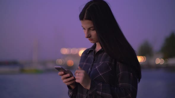 Woman Walking on Quay with Phone in Hands Texts with Cellphone on Night Street