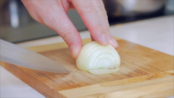Close-up Woman's Hand Cuts Onion Into Rings on a Split Board at Home in Her Kitchen. alt