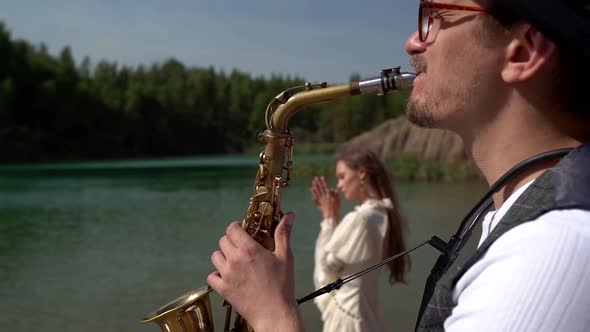 a Saxophonist Plays a Soulful Composition for His Girlfriend in Nature Near a Forest Lake alt