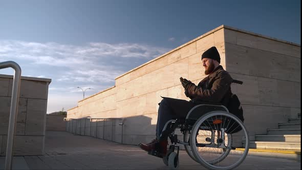 Physical Disability and Trouble with Moving in City Man in Wheelchair is Using Smartphone alt