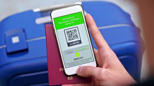 Male hand holding passport and smartphone with International Vaccination Certificate COVID-19 QR cod alt